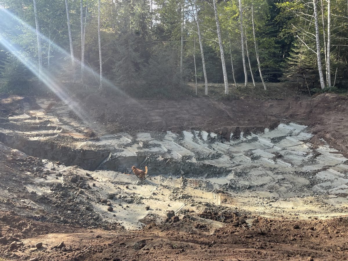 Excavator at the bottom of the 18 to 20 foot deep pond excavation, showing full depth and scale of the dig