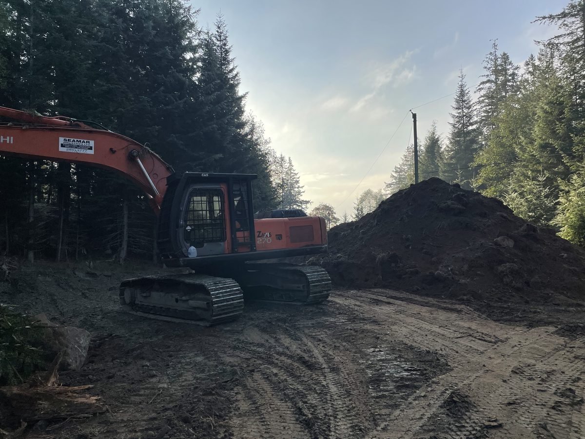 Hitachi excavator working at the edge of the pond excavation, spoil material visible on surrounding grade